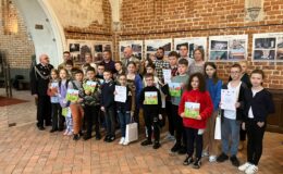 stoi grupa osób, dorośli, dzieci, młodzież, pozują do pamiątkowej fotografii w sali zamkowej